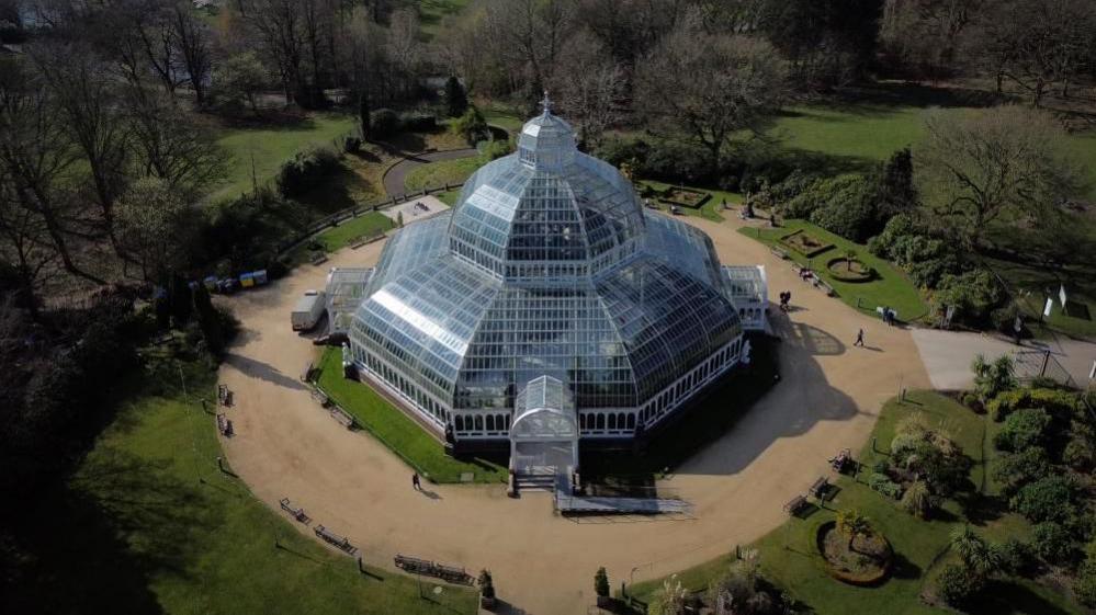 An aerial shot of the Palm House, a domed glass conservatory surrounded by parkland in Sefton Park.