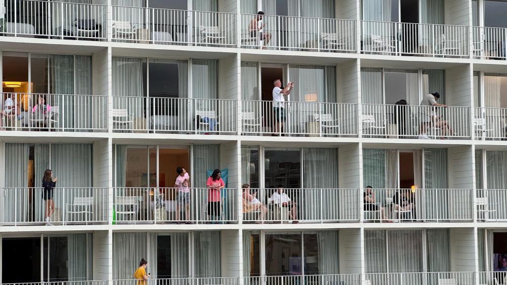 Many hotel balconies with people standing on them, some taking photos.