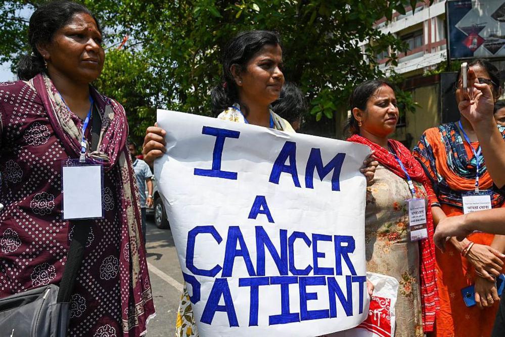 A woman who is a cancer survivor and a teacher participating in a demonstration in Kolkata in April 2025, holding a "I am a cancer patient" placard. 
