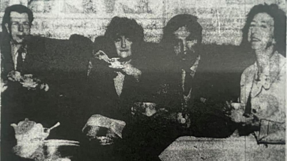 A grainy black and white photo of four people sitting on a sofa