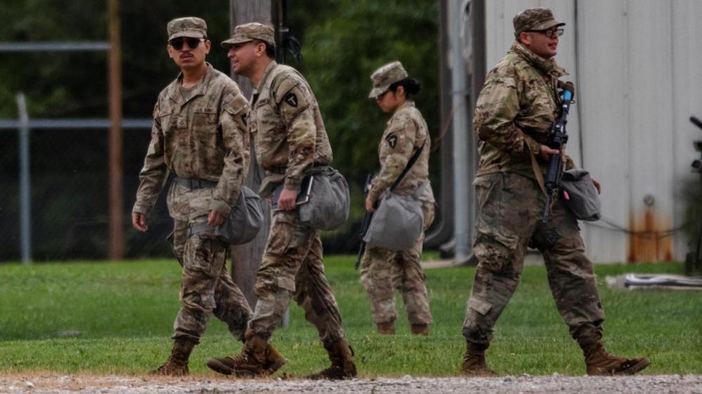 Four national guard troops from Texas are wearing camouflage uniforms and walking on grass