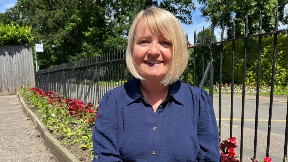 Headteacher Jo Snelling standing by a floral display and iron railings