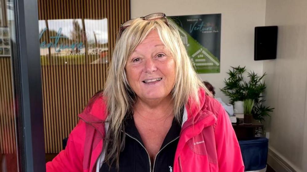 Jackie Leek smiling opening a door wearing a black top and salmon-coloured jacket