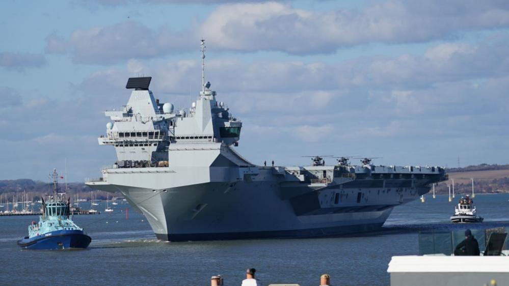 A large military ship on the ocean with two smaller ships on the water on either side