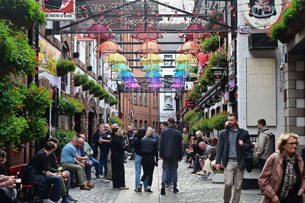 A number of people stand underneath colourful, neon umbrellas, in Belfast's commercial court. 