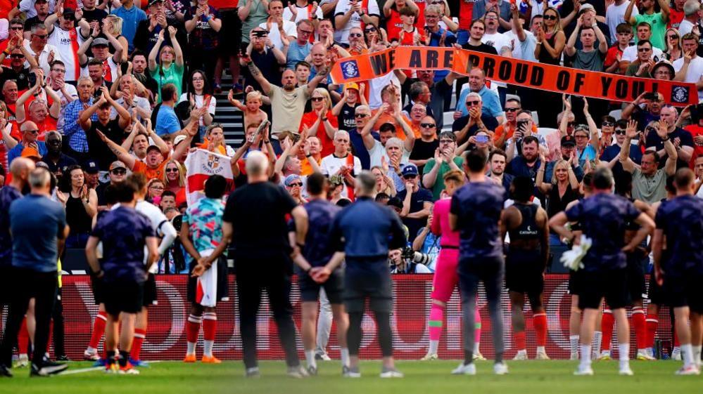 Fans in the stands at the London Stadium applauding Luton Town players who are lined up in front of them