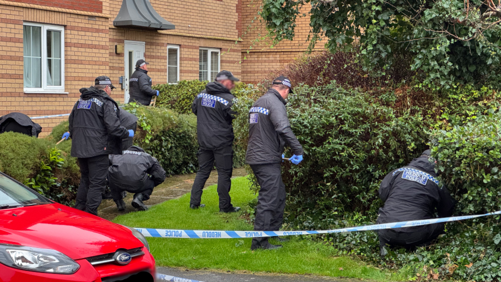 Police officers search a garden area in Grangetown, Cardiff, with police tape cordoning it off