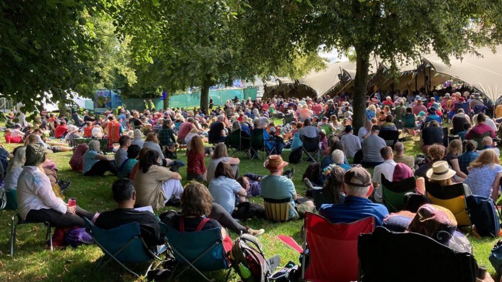 Crowd of people sitting on grass in front of a stage