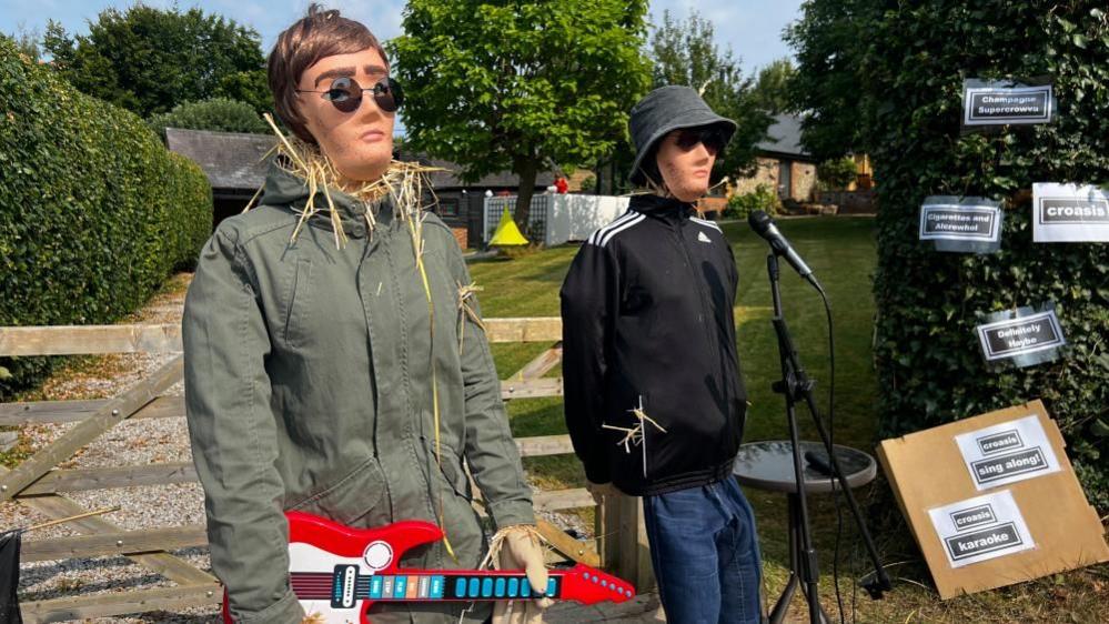 Liam and Noel Gallagher, as scarecrows, with guitar and microphone