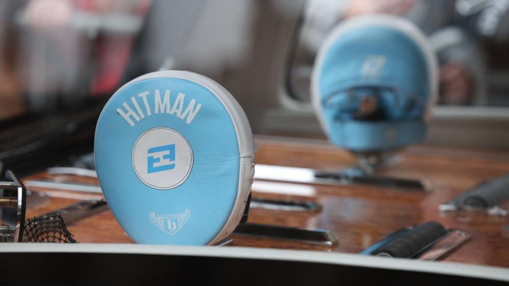 Two blue boxing pads with the word 'Hitman' on them are displayed upright in inside the back of a car.