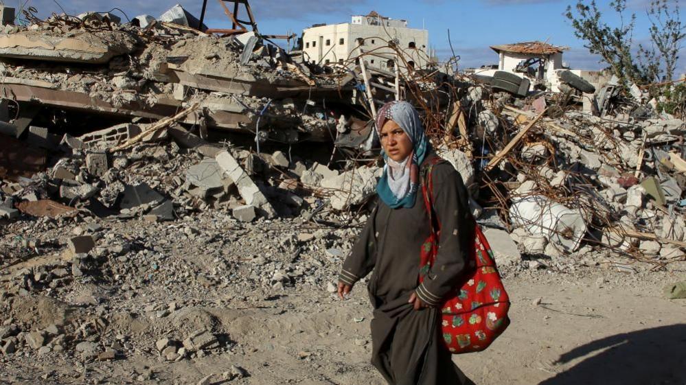 A Palestinian woman walks past the rubble of houses and buildings destroyed during the war, following a ceasefire between Israel and Hamas, in Rafah in the southern Gaza Strip, January 20, 2025