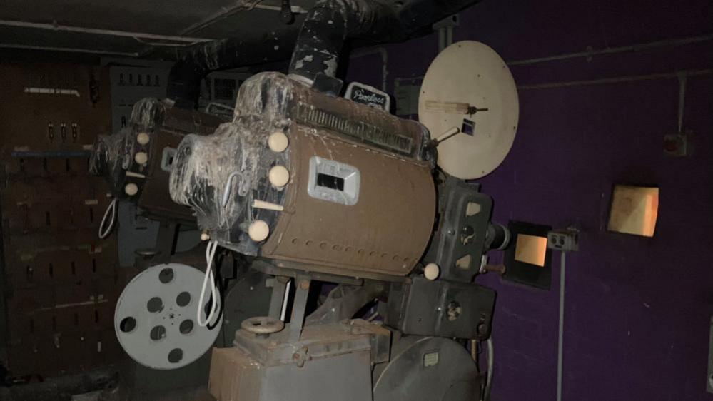 A broken a disused film projector covered in dust.