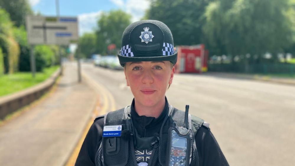 Insp Davis-Lyons in police uniform standing in a road with police cars in the background