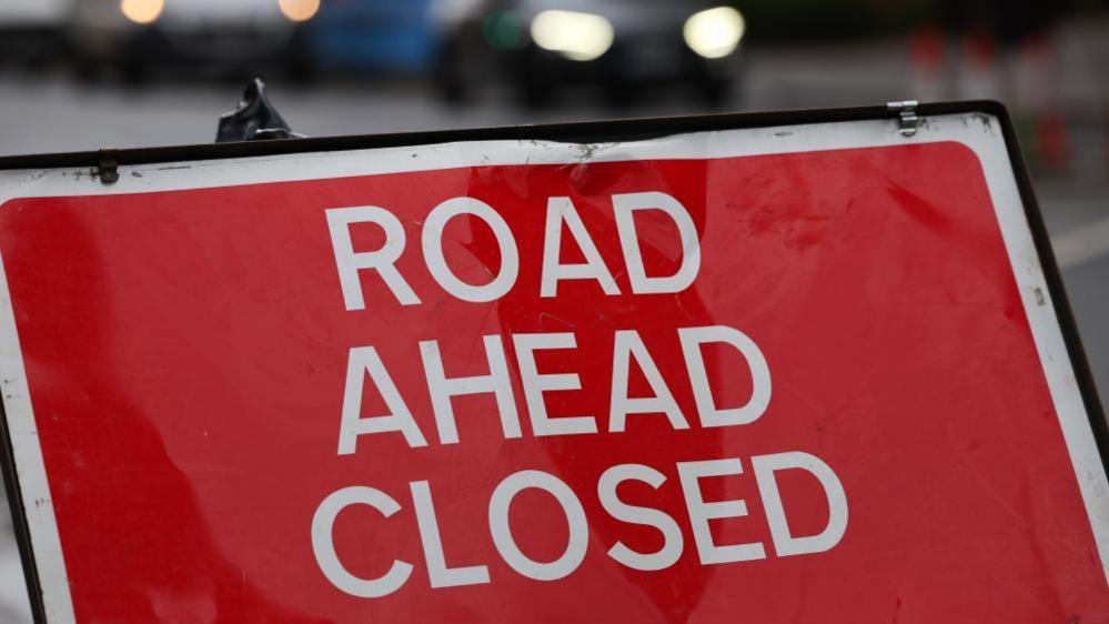 A red sign with white writing reads road ahead closed