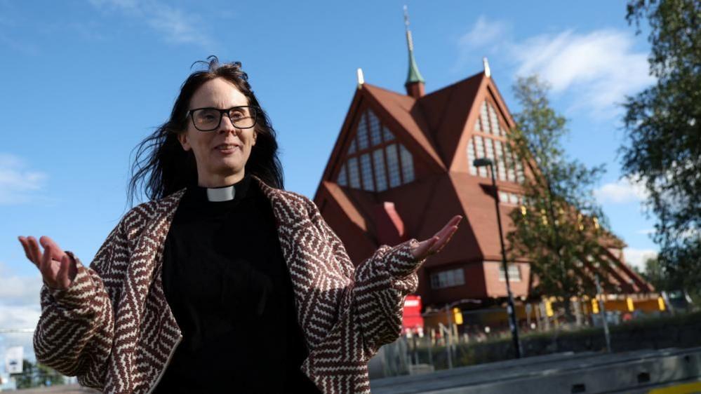 Pastor Lena Tjarnberg, speaks during an interview in front of Kiruna's historic wooden church, before it is moved to its new site