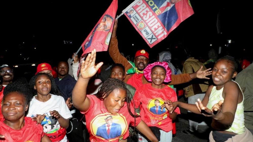 Supporters of Zambia's President Hakainde Hichilema celebrate, wearing T-shorts with his umage on.