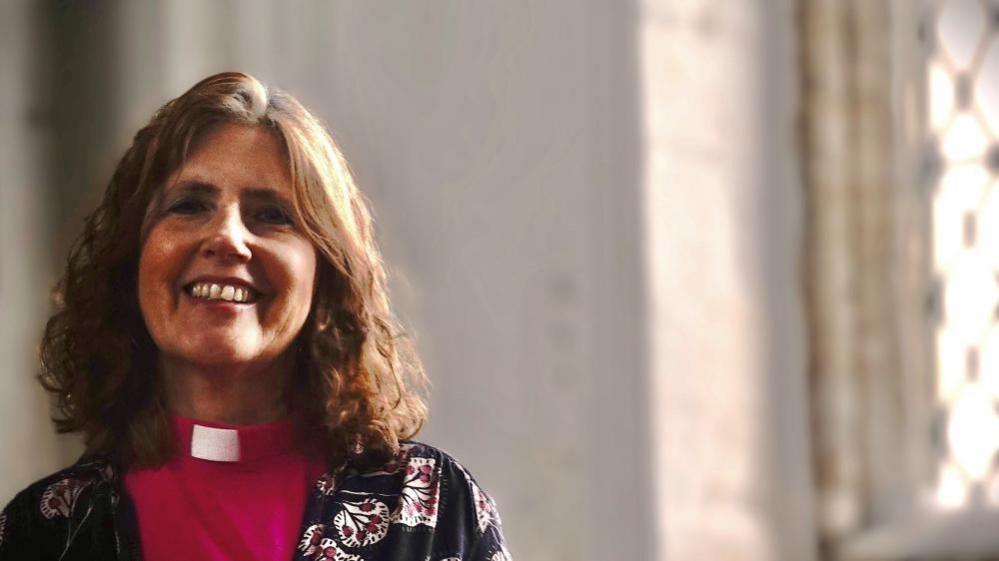 Vicar Ruth Clay wear pink cassock and floral patterned cardigan 