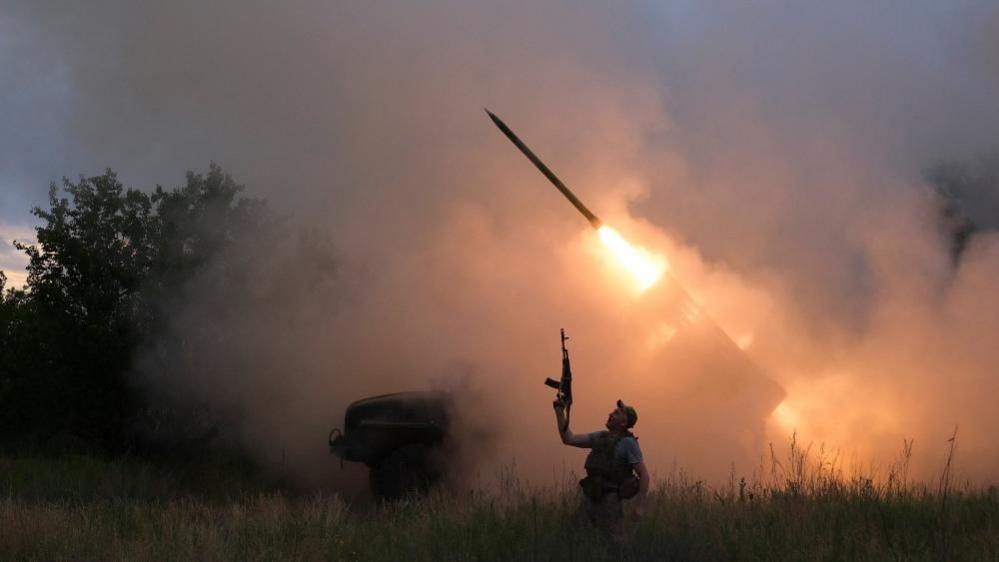 A Ukrainian soldier from the 93rd Kholodnyi Yar Separate Mechanized Brigade of the Ukrainian Armed Forces reacts as his colleagues fire a BM-21 Grad multiple launch rocket system towards Russian troops