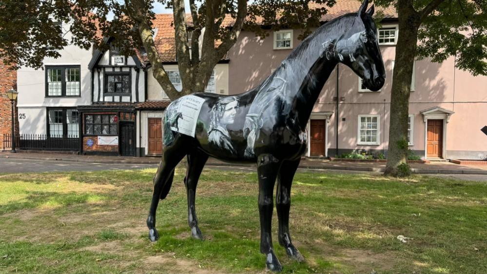A fibre-glass horse, painted with images of Black Beauty author Anna Sewell, and her work. Behind the rear end of the horse is Anna Sewell House, where the writer was born.