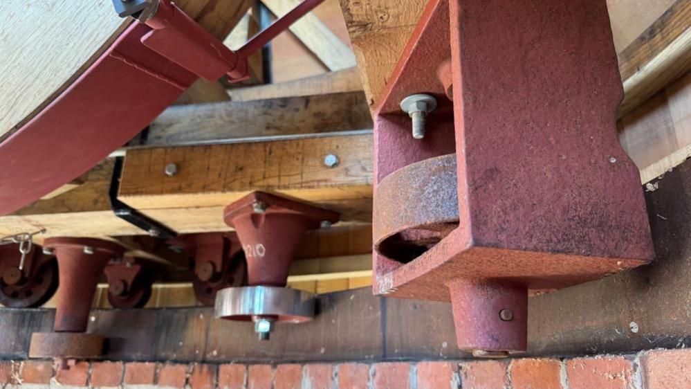Cast iron fittings, painted in red oxide paint, with some surfaces shiny owing to machining through the refurbishment process. The wheels are set into an oak frame, within the cap of the wind pump.