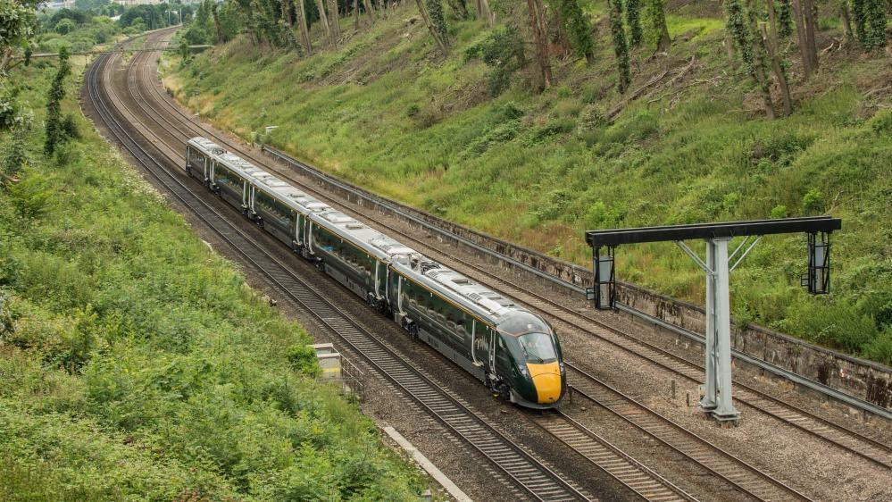 A green GWR train passing through a green wooded valley