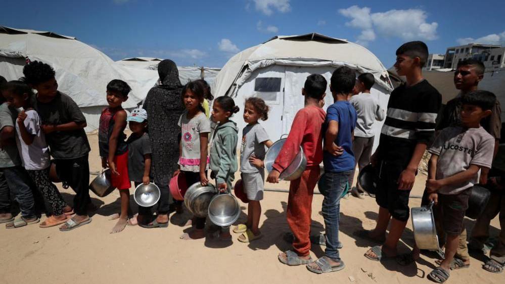 Displaced children queue for food at a charity kitchen in Gaza City