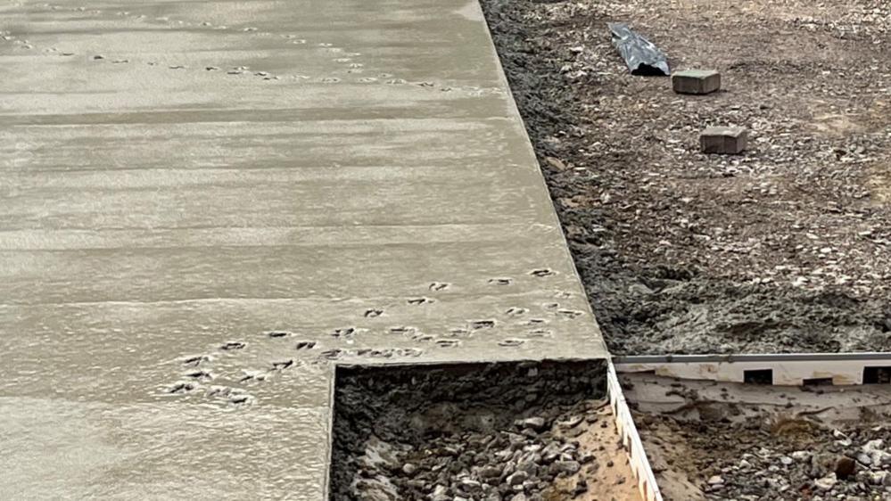 Footprints in wet concrete, with the area to the right and in the mid foreground awaiting concrete or other surfacing to be installed.