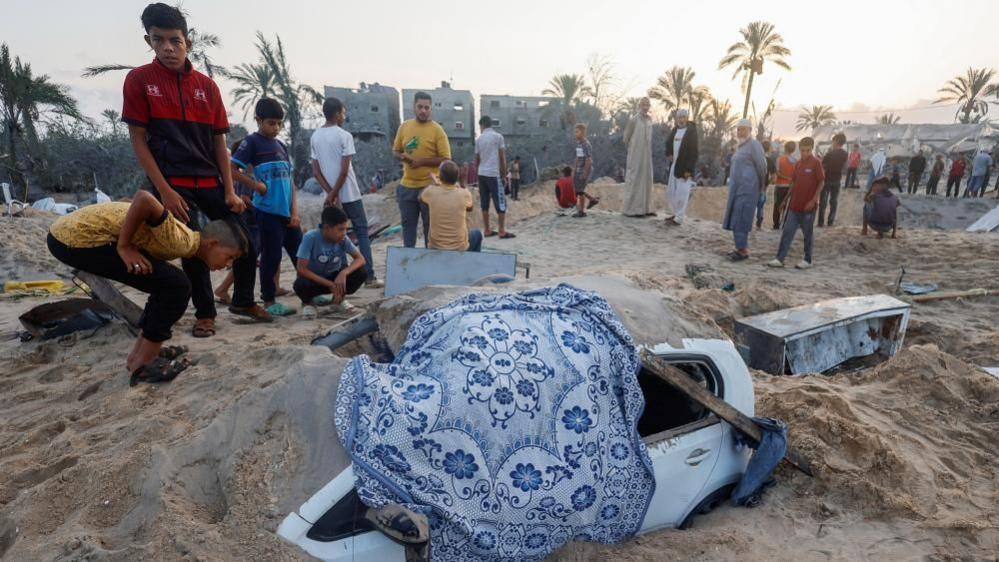 Palestinian boys inspect a vehicle buried in sand following an apparent Israeli air strike on a camp in southern Gaza