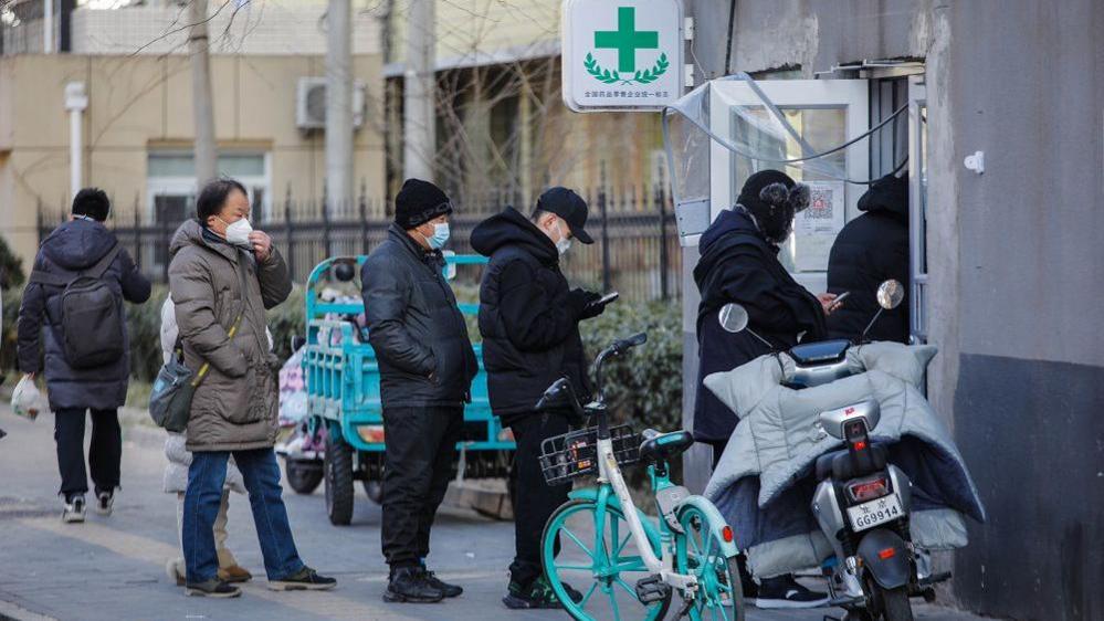 People wearing masks queuing outside a pharmacy