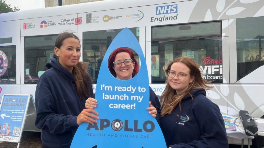 Darby, left, and Lucy, right, with their tutor Louise Frosdick visible through an aperture in an advertising board cut to the shape of a rocket, stating: "I'm ready to launch my career."