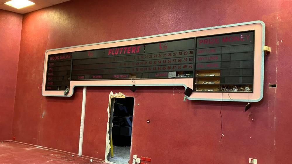 The broken and disused bingo number screen on a red wall.