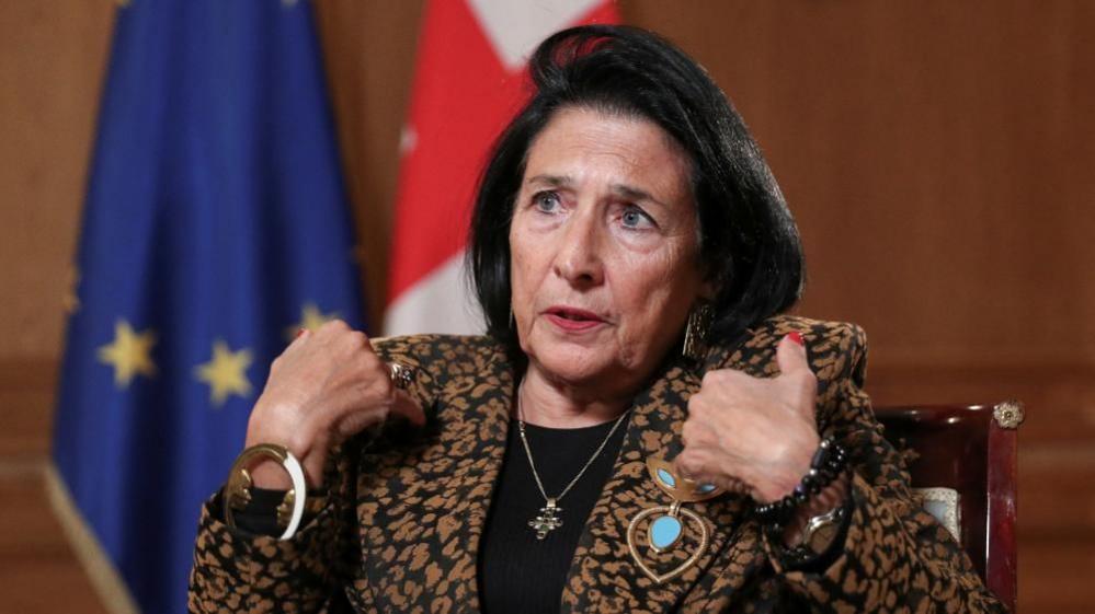 Georgia's President Salome Zourabichvili gestures during an interview as she sits in front of her country's flag and the EU flag