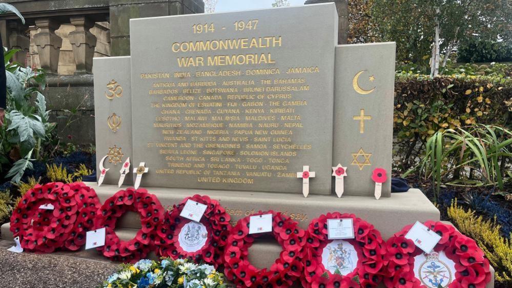 A stone memorial stone with gold writing surrounded by red poppy wreaths.