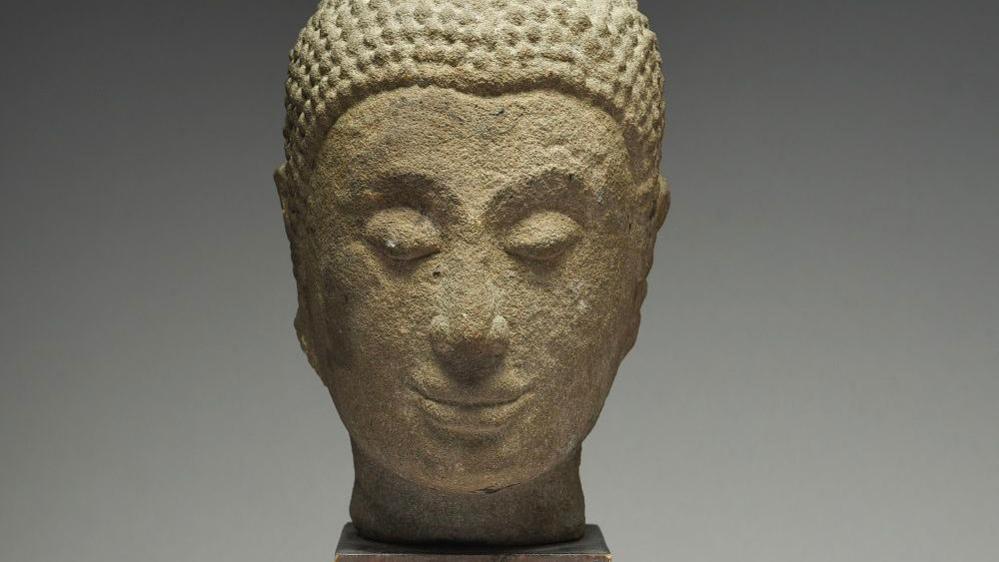 A slightly worn stone head depicting the Buddha - eyes closed and smiling.