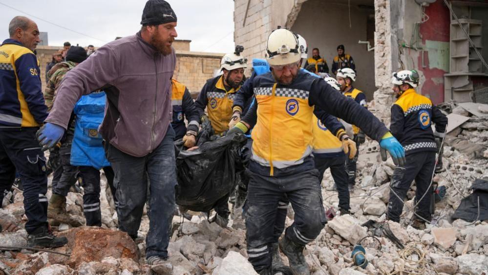 Rescuers carry a body bag across rubble