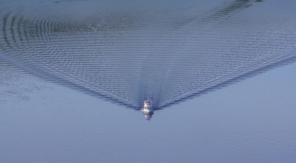 A boat sails across the calm blue water creating ripples behind it