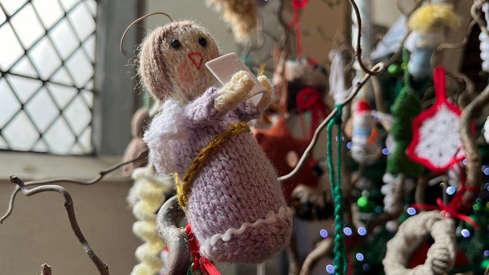 A knitted singing angel hanging off the branch of a stick