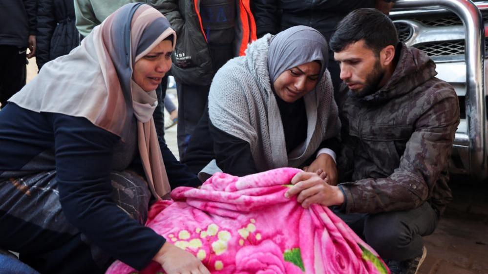 Mourners crouched with the covered body of a Palestinian killed in an Israeli air strike in Gaza (03/01/25)