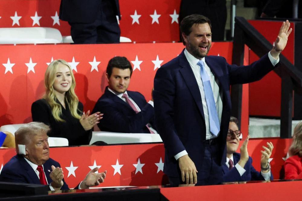 Republican vice presidential nominee JD Vance seen waving to the crowd at the Republican National Convention. Trump is seen set beside him applauding.