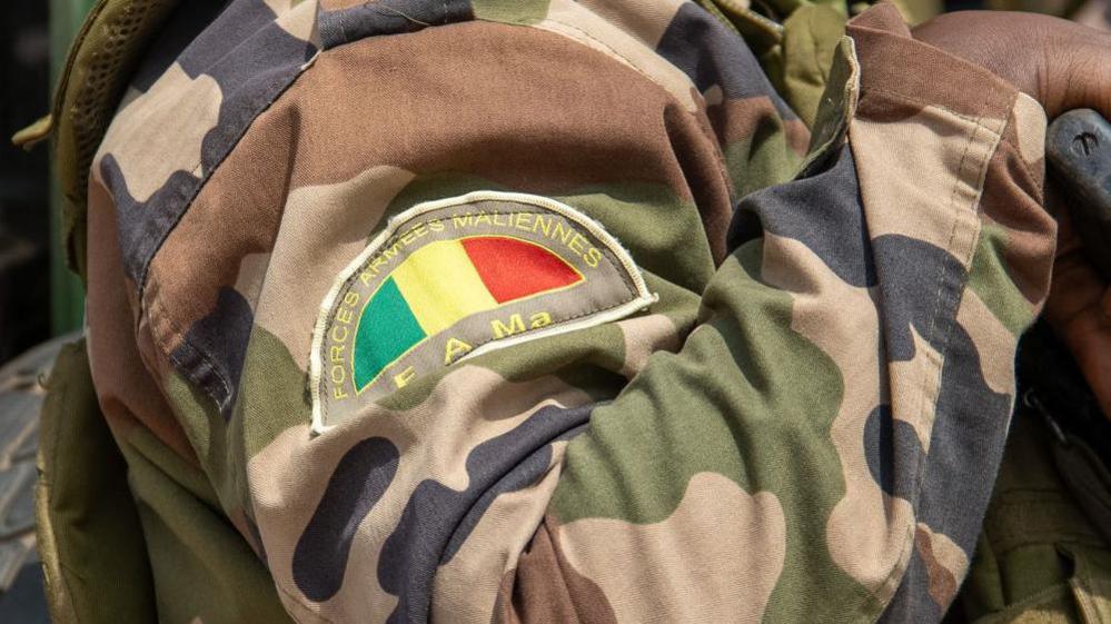 A close up of a Mali army badge on the shoulder of a camouflage uniform.