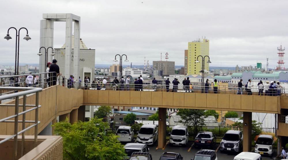 People standing on a raised pedestrian overpass, which is on top of a carpark. They are looking out over the city.