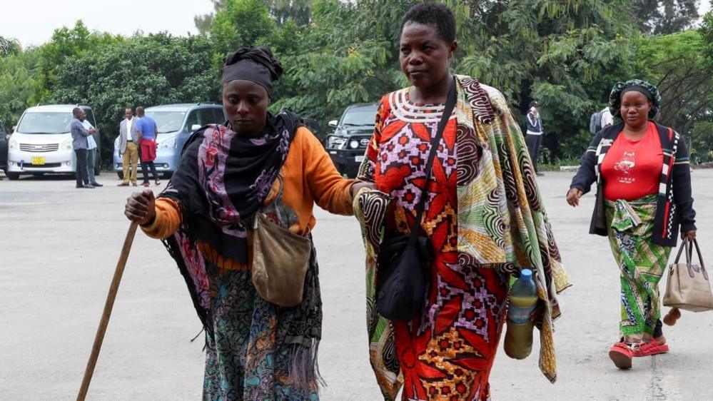 Three women, one with a walking stick, at DR Cong' border with Rwanda