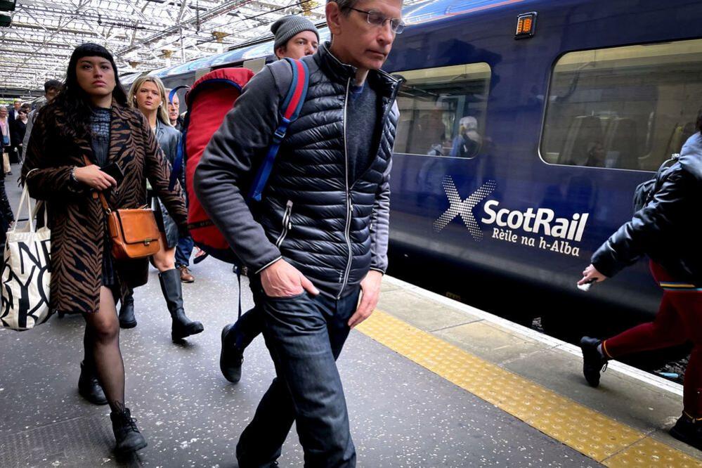 People walk on the platform at Glasgow Central by a ScotRail train