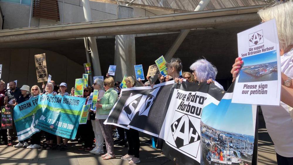 Campaigners line up outside the Scottish Parliament building holding signs which say 