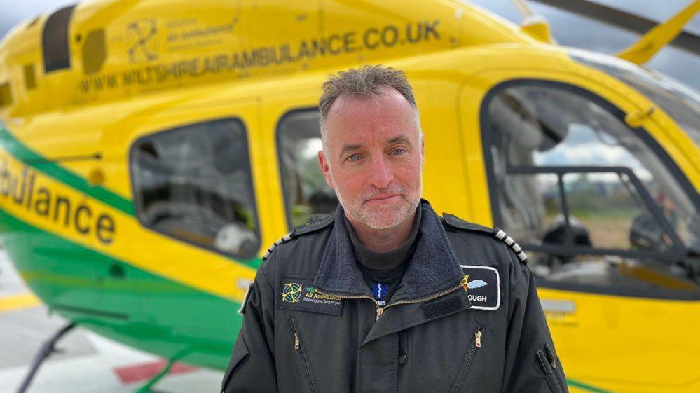 Captain Simon Gough looks into the camera in front of the helicopter