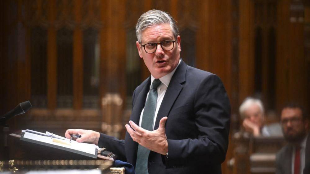 Keir Starmer speaking at the despatch box the House of Commons, he has a folder with notes and a microphone in front of him