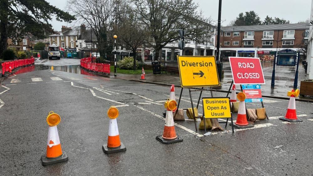 A road closure in Chalfont St Peter, Buckinghamshire, showing cones, water on the road and a diversion and road closed sign.