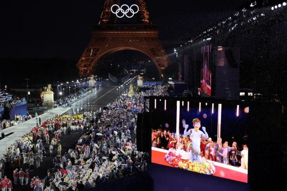 Delegations arrive at the Trocadero as spectators watch French singer Philippe Katerine performing on a giant screen during the opening ceremony of the Paris 2024 Olympic Games on 26 July 2024 