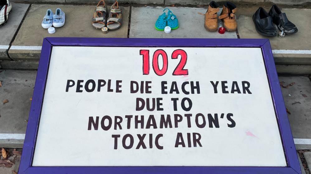 White banner with black writing saying that 102 people die from Northampton's toxic air