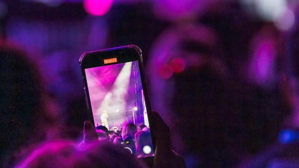 A photo of someone taking a video of a singer, Tom Grennan. He isn't visible.